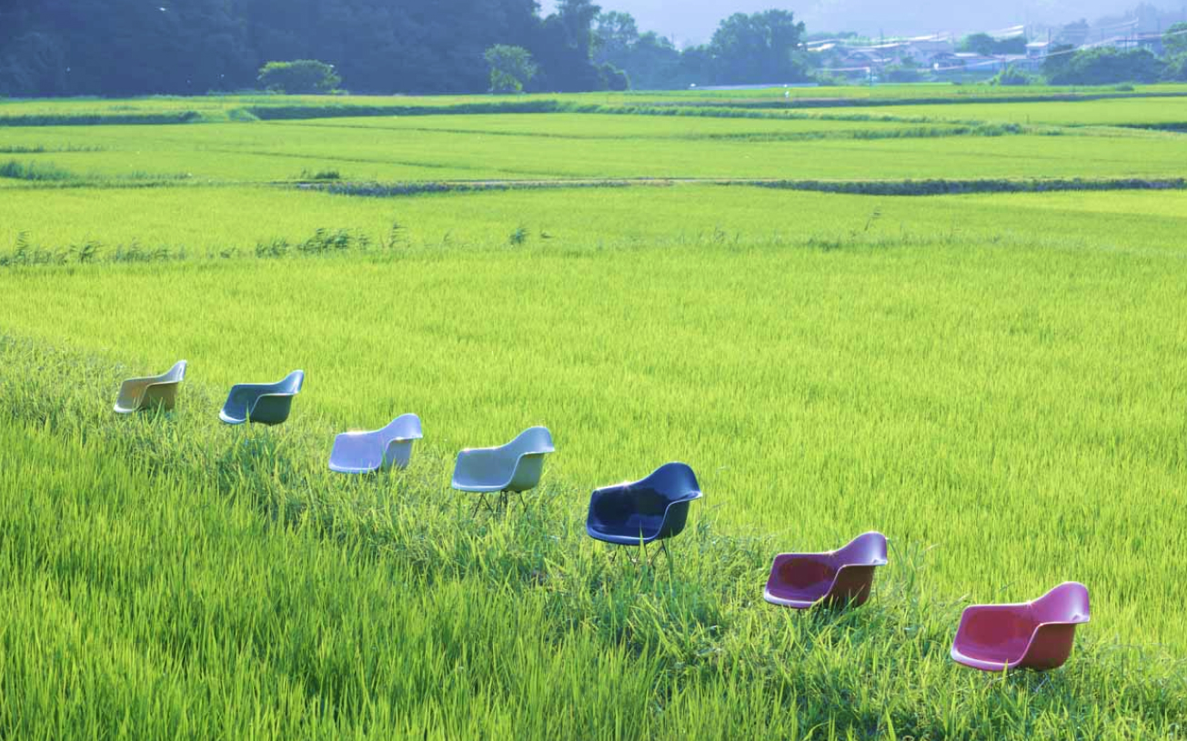 田園風景に置かれた丸に三つ石の「イームズ リプロダクトチェア」